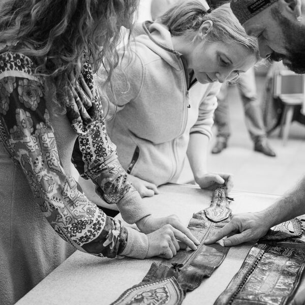 Three seminar participants inspect the workmanship of an old leather belt decorated with quill embroidery, which lies spread out on the table in front of them.