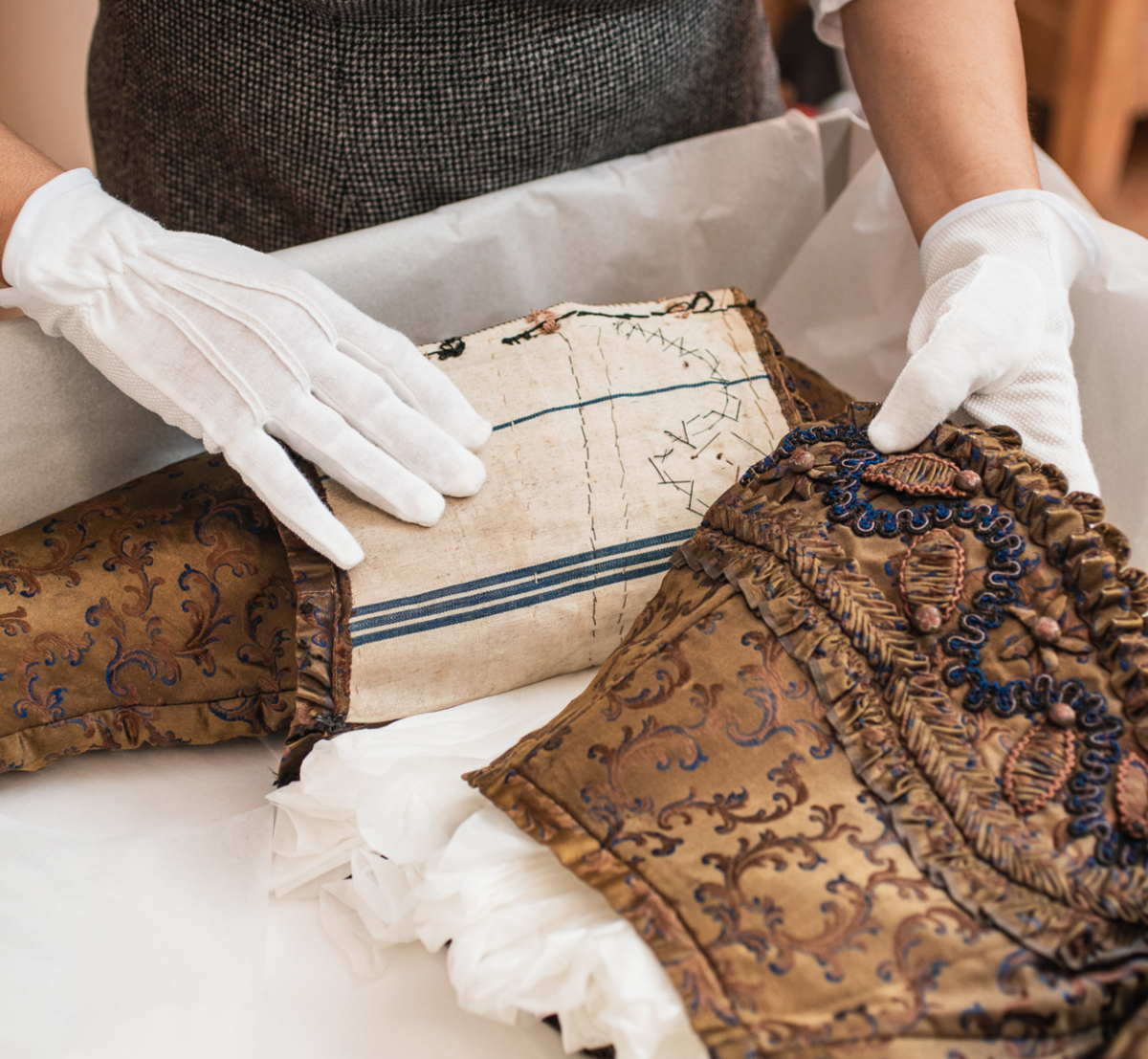 Mit weißen Handschuhen verpackt eine Archivarin ein historisches Damenoberteil in Seidenpapier.