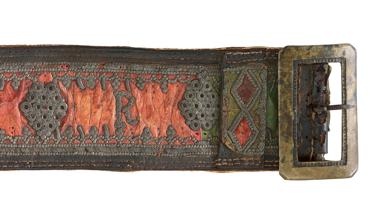 Detail eines braunen Ledergürtels mit Zinn-Nieten und rötlichem Textil sowie einer Messingschnalle. Die Archivalie, datiert 1804, stammt aus Oberbayern.