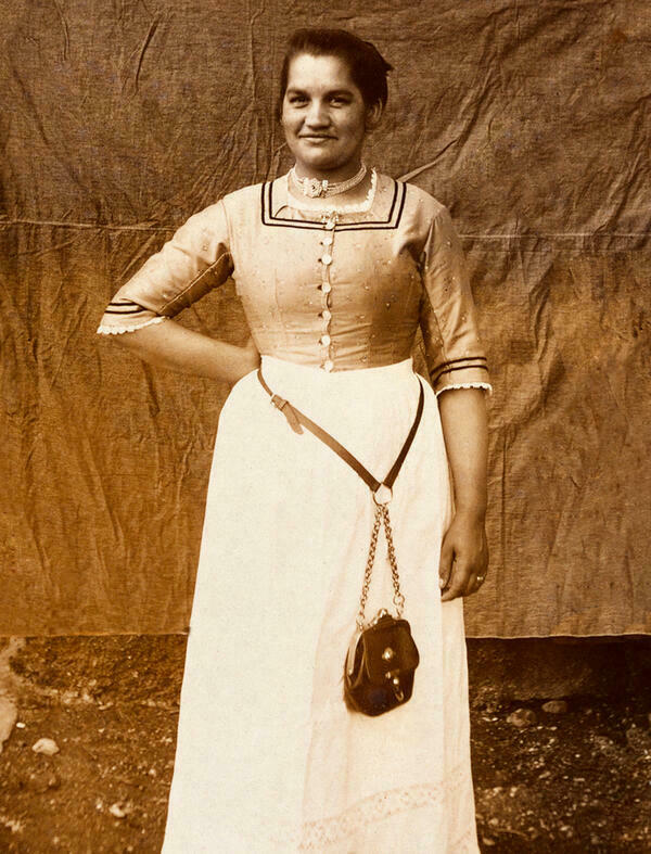 Black and white photograph of an Upper Bavarian waitress around 1910. The waitress's bag hangs on the belt of the dirndl in her waistcoat.